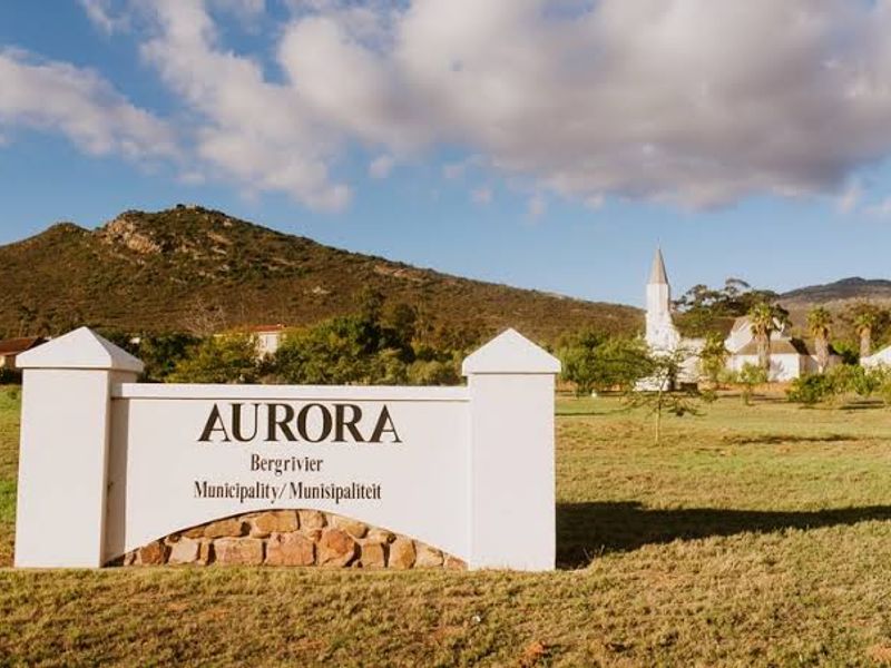 A view of the Aurora town entrance sign featuring stone-clad masonry and concrete pillars set against a scenic mountain landscape.