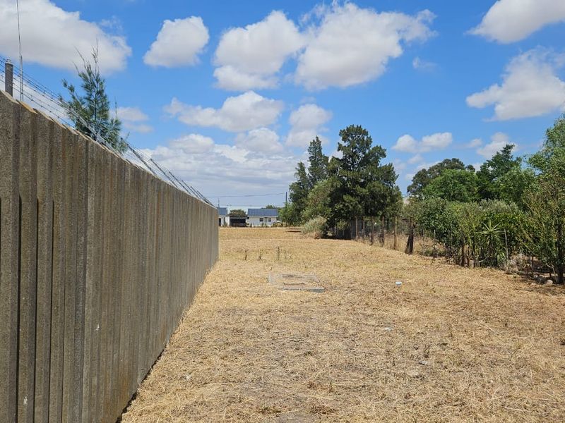 A vacant residential plot featuring a precast concrete boundary wall with electric fencing and established perimeter vegetation.