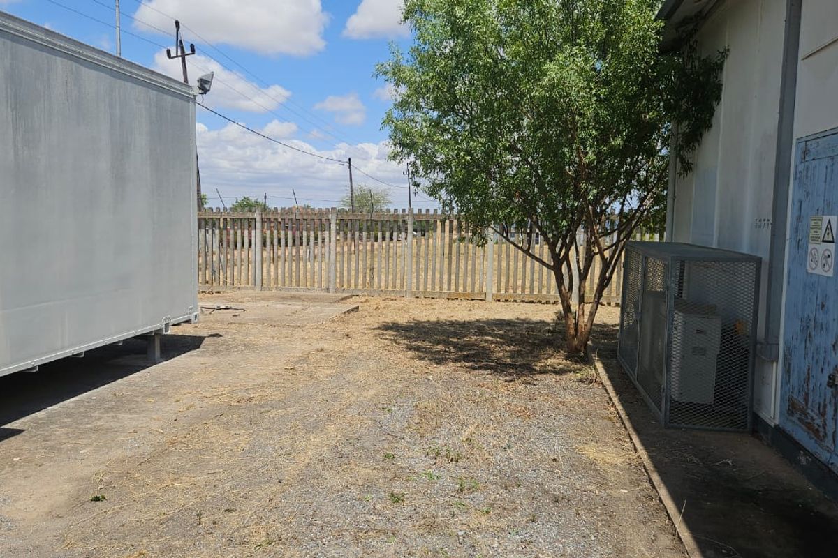 Rear exterior area featuring gravel ground cover, concrete palisade fencing, and a metal security cage enclosure against the building wall.