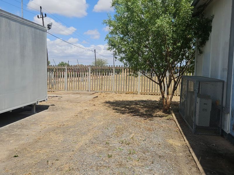 Rear exterior area featuring gravel ground cover, concrete palisade fencing, and a metal security cage enclosure against the building wall.