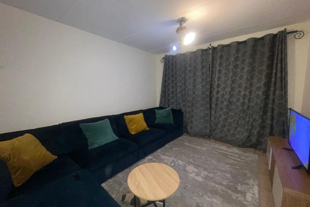 A comfortable living room space featuring neutral walls, tiled flooring, and full-length curtains covering the window area.