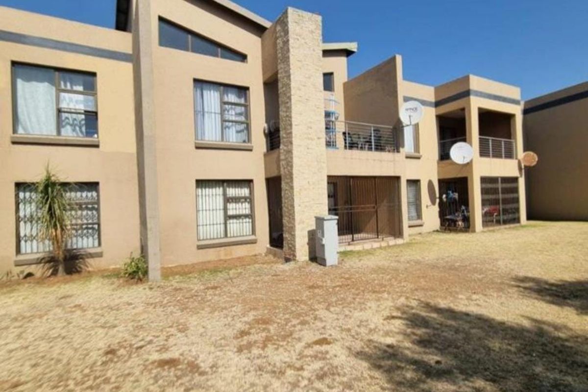 Rear view of a multi-story apartment complex featuring stone cladding accents, private balconies, and security bars on windows, set against a dry lawn area.