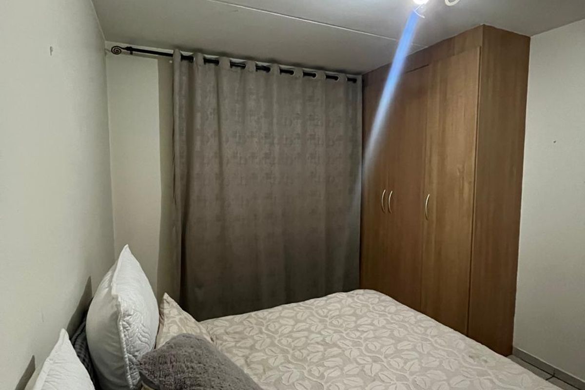A functional bedroom featuring a built-in wooden wardrobe, neutral wall finishes, and a curtained window.
