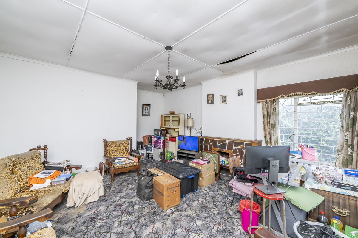 Living room featuring a stone fireplace, chandelier, and security bars on the window. The space requires ceiling repairs and flooring updates.