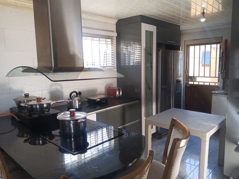 A functional kitchen featuring granite countertops, modern cabinetry, a stainless steel extractor fan, and direct access to the exterior via a security gate.