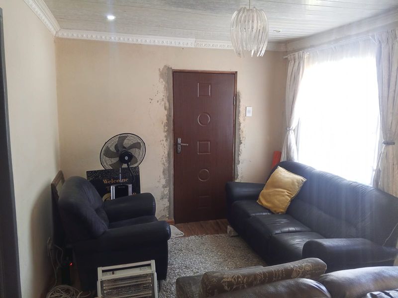 A living room featuring a timber ceiling and crown molding, currently showing visible wall damage around the door frame requiring repair and cosmetic attention.