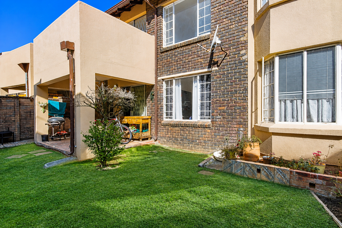 Rear view of the townhouse featuring a private garden, a covered patio area, and a combination of brick and plastered exterior finishes.