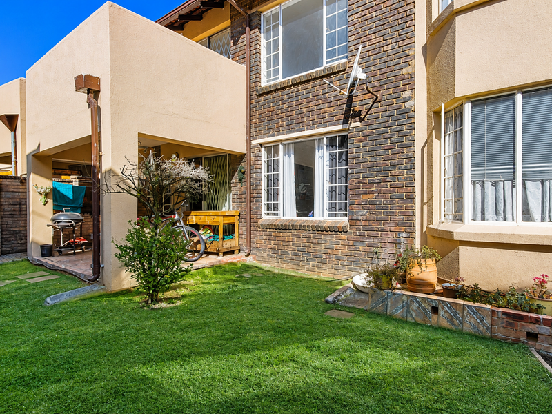 Rear view of the townhouse featuring a private garden, a covered patio area, and a combination of brick and plastered exterior finishes.