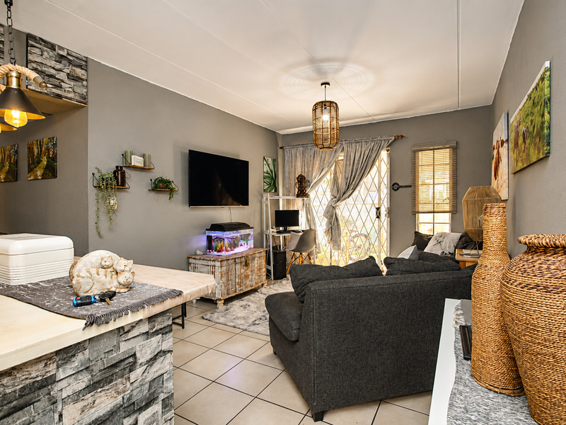 Open-plan living area featuring tiled flooring, a stone-clad kitchen counter, and direct access to the exterior through a sliding security gate.