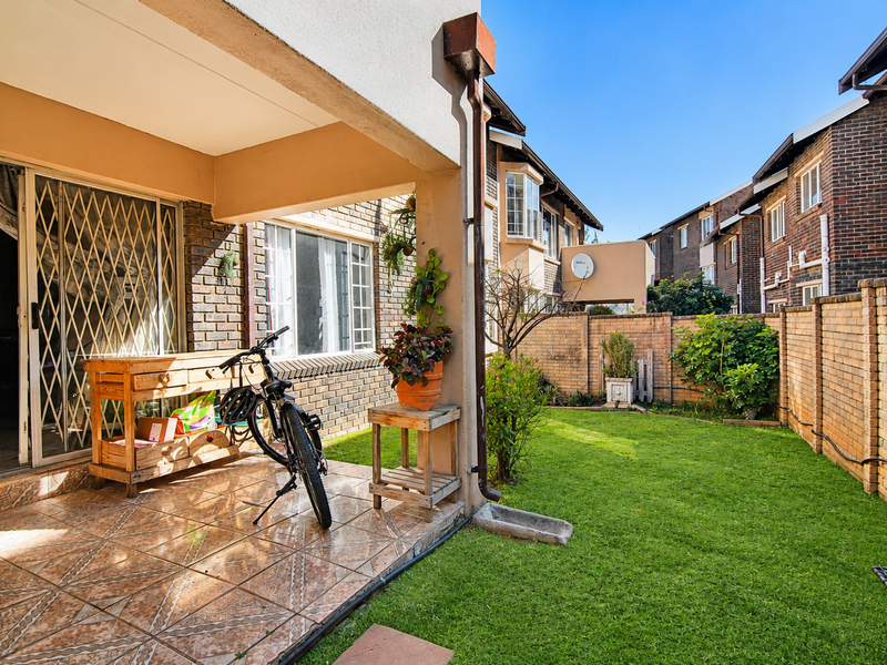 A covered patio area with tiled flooring and a security gate, leading out to a private garden enclosed by brick boundary walls.