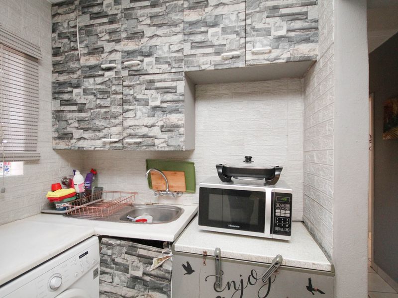 Compact scullery area featuring built-in cabinetry, a stainless steel sink, and laminate countertops, requiring some maintenance and cosmetic updates.