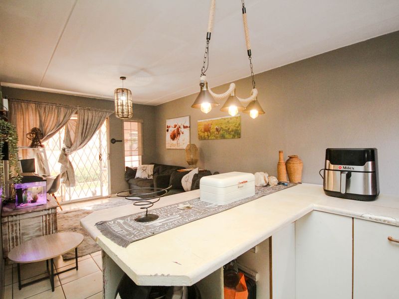 Open-plan living area featuring a kitchen island with breakfast counter, tiled flooring, and direct access to the patio through a security sliding door.