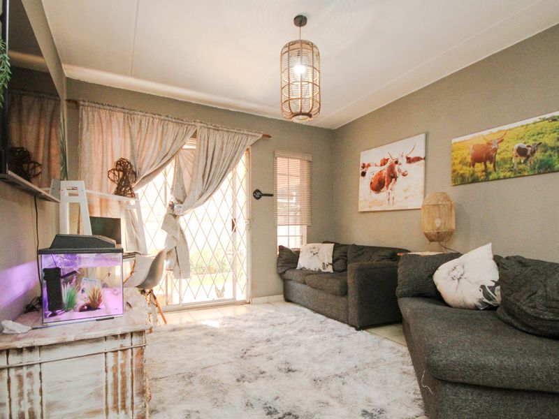A comfortable living room featuring tiled flooring, a sliding glass door with security gate, and neutral wall tones, providing a functional and inviting space.