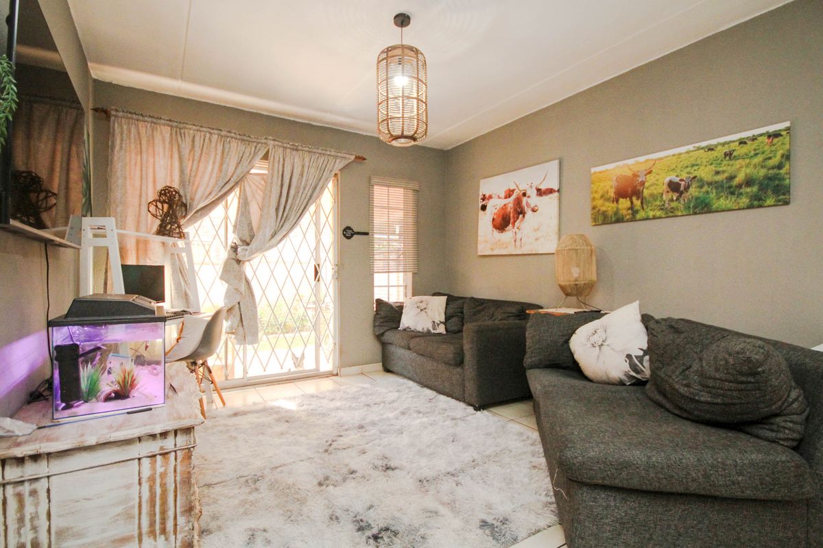 A comfortable living room featuring tiled flooring, a large sliding glass door with security gate, and neutral wall tones.
