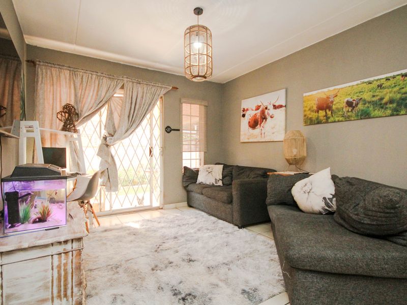 A comfortable living room featuring tiled flooring, a large sliding glass door with security gate, and neutral wall tones.