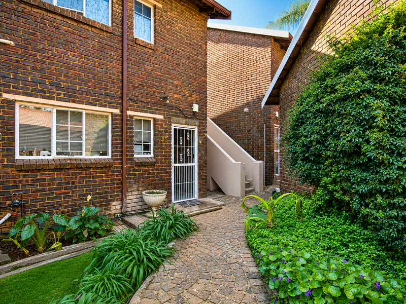Front entrance of a face brick townhouse featuring a paved walkway, security gate, and external staircase leading to upper levels.