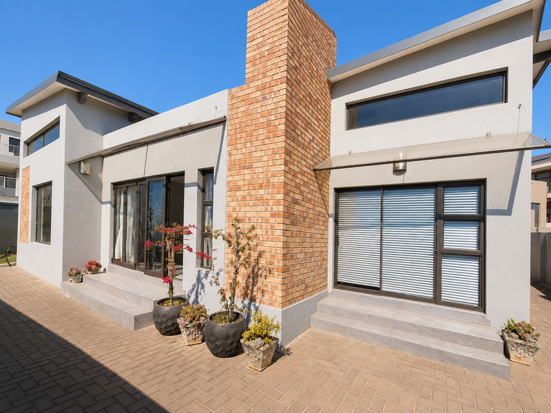 Modern rear exterior featuring a prominent brick chimney, paved patio area, and large sliding glass doors providing seamless indoor-outdoor flow.