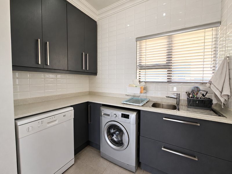 Modern laundry room featuring dark cabinetry, stone countertops, subway tile backsplash, and integrated space for appliances.