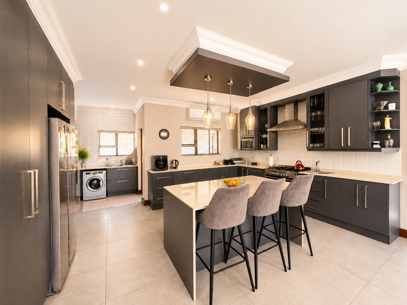 Modern open-plan kitchen featuring dark cabinetry, a central island with breakfast seating, stone countertops, integrated appliances, and a dedicated laundry area.