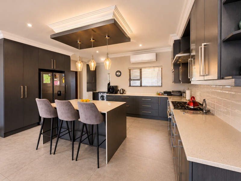 Modern kitchen featuring dark cabinetry, quartz countertops, a central island with pendant lighting, subway tile backsplash, and integrated appliances.
