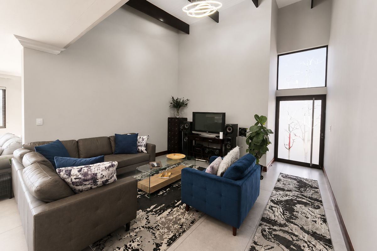 Spacious living room featuring high vaulted ceilings with exposed timber beams, large windows for natural light, and neutral tiled flooring.
