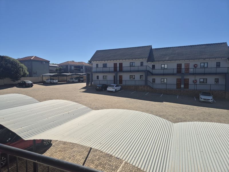 Exterior view of an apartment complex featuring a paved parking area with covered carports and multi-story residential units.