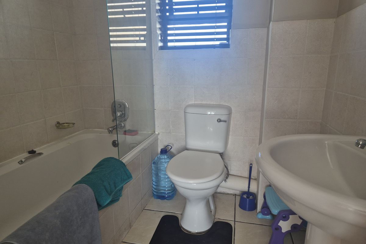 A functional bathroom featuring a bathtub with a glass screen, a pedestal basin, and a toilet, finished with neutral wall and floor tiles.