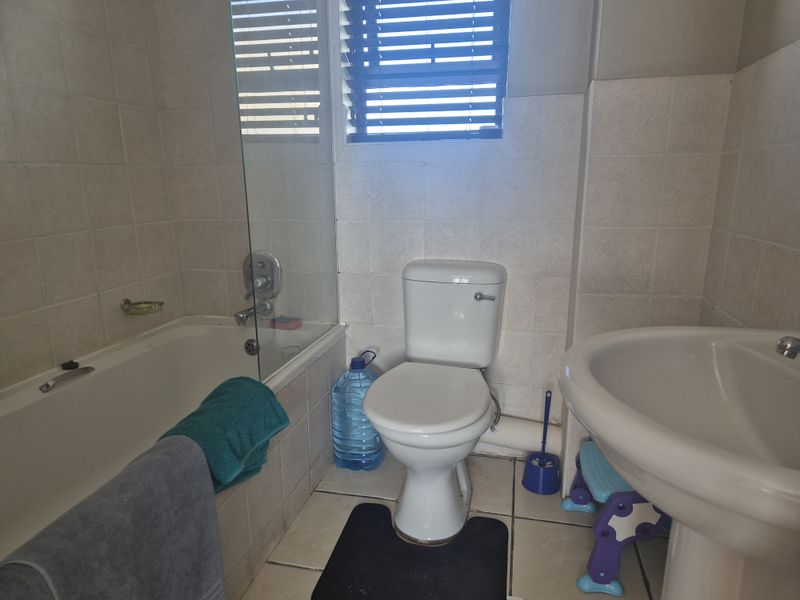 A functional bathroom featuring a bathtub with a glass screen, a pedestal basin, and a toilet, finished with neutral wall and floor tiles.