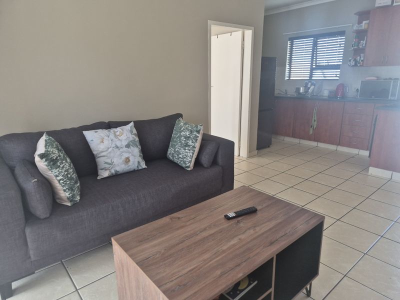 Open plan living area featuring tiled flooring and a functional kitchen with built-in cabinetry and venetian blinds.