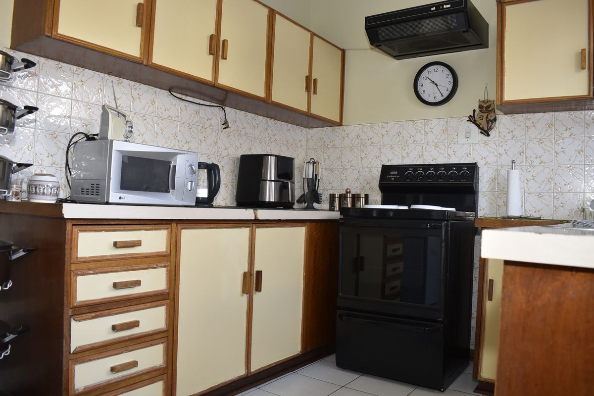 A functional kitchen featuring dated cabinetry, a tiled backsplash, and a black freestanding stove with an overhead extractor fan.