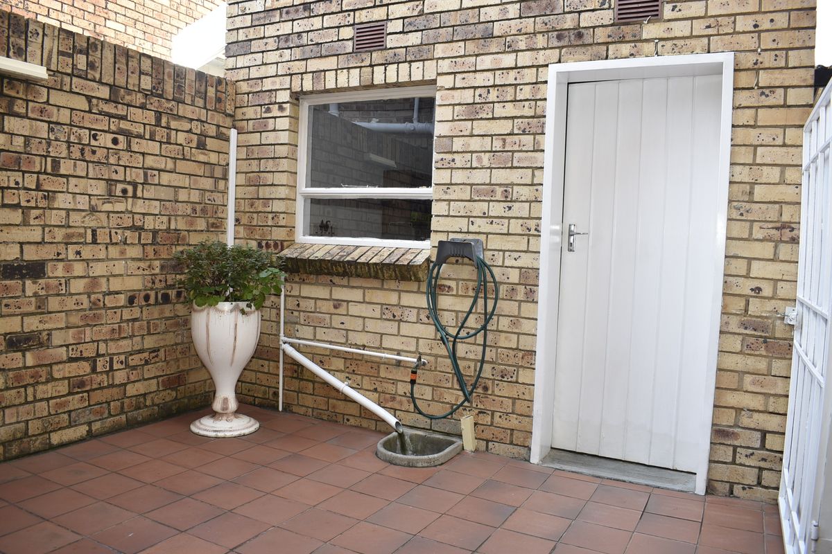 A paved rear courtyard area featuring face brick walls, an external door, and basic utility plumbing fixtures.