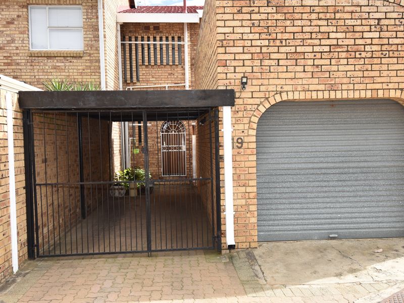 Front elevation of a townhouse featuring a face brick facade, a secure roller shutter garage, and a covered carport entrance.