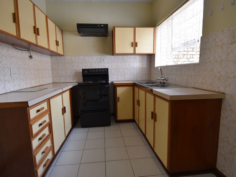 A functional kitchen featuring original cabinetry, laminate countertops, a freestanding stove, and tiled splashbacks, offering potential for a modern renovation.