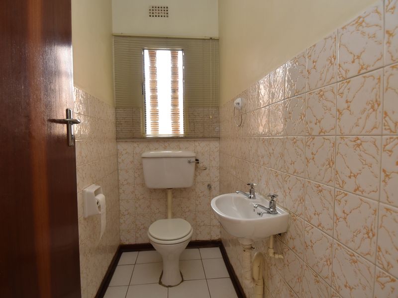 A compact guest bathroom featuring dated wall tiles, a wall-mounted basin, and a standard toilet, offering potential for a modern renovation.