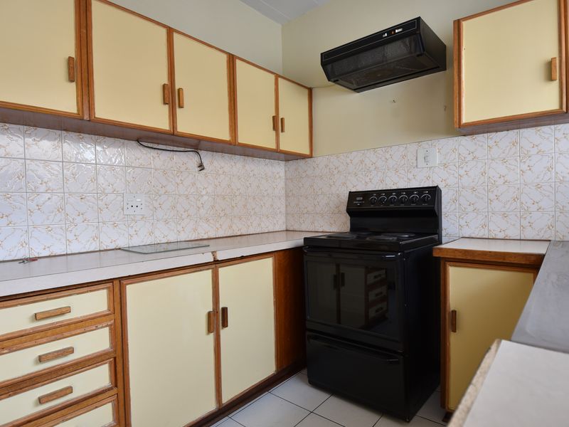 A functional kitchen featuring dated cabinetry, tiled backsplash, and a freestanding electric stove with an extractor fan.