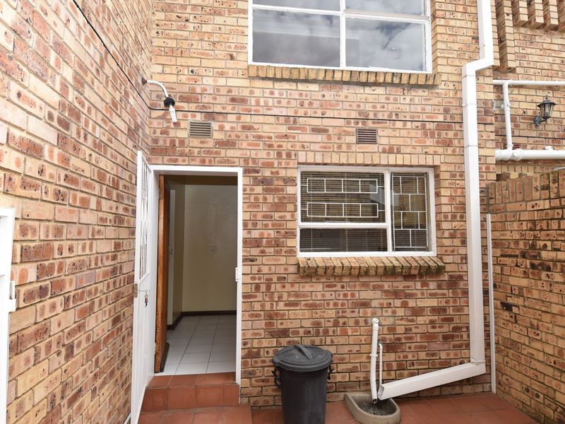 Rear exterior view of the townhouse featuring face brick walls, a tiled patio area, and secure window bars.