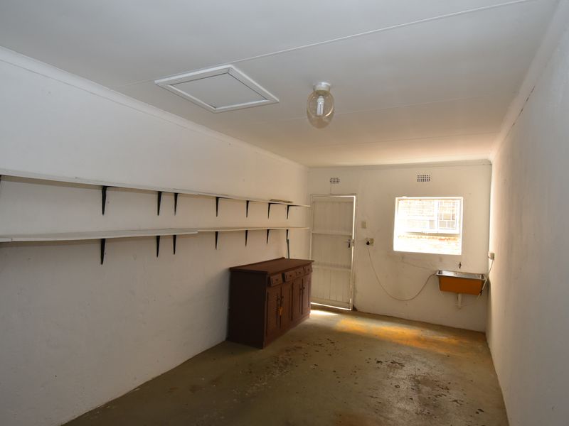 A functional utility or storage room featuring wall-mounted shelving, a basic utility sink, and direct access to the exterior.