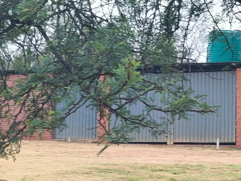 A functional farm utility building constructed with brick and corrugated metal, featuring an integrated water storage tank.