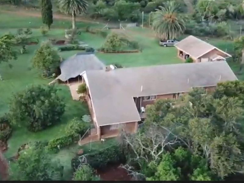 Aerial view of a farm property featuring a main dwelling, a detached garage, and a thatched roof lapa set within a spacious landscaped garden.