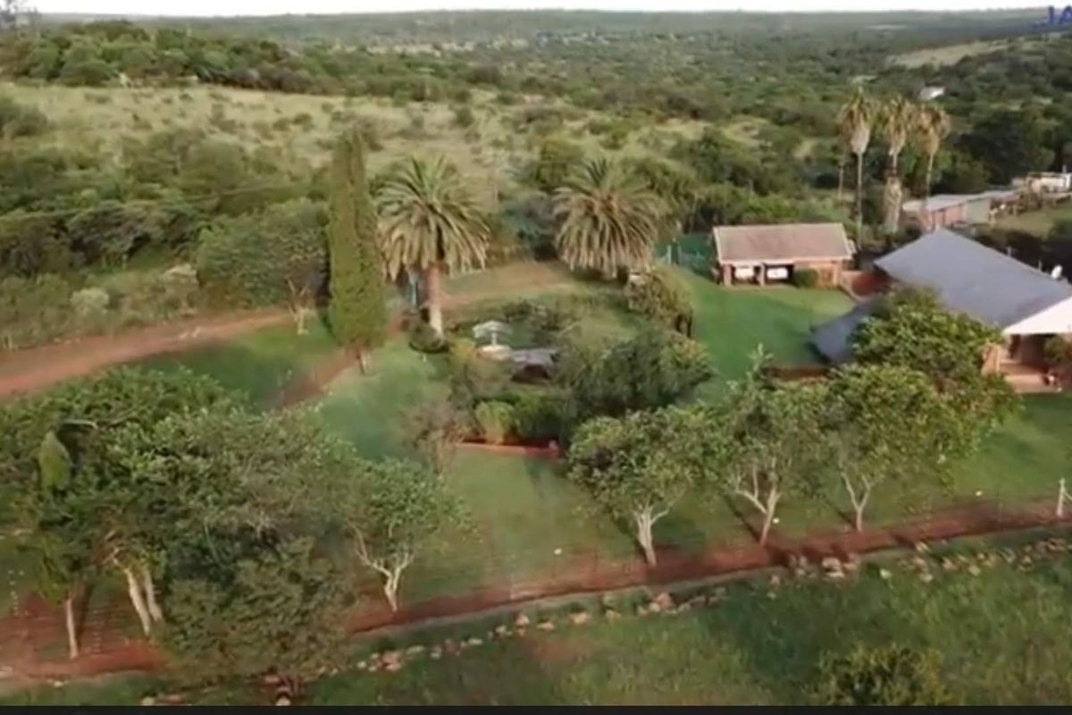 Aerial view of a farm property featuring a main residence, outbuildings, expansive green lawns, mature trees, and surrounding rural landscape.