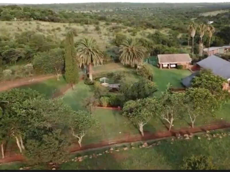 Aerial view of a farm property featuring a main residence, outbuildings, expansive green lawns, mature trees, and surrounding rural landscape.