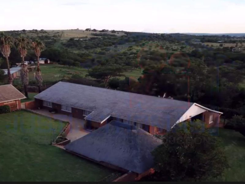 Aerial view of a farm property featuring multiple buildings with tiled and thatched roofs, surrounded by expansive lawns and rural landscape.