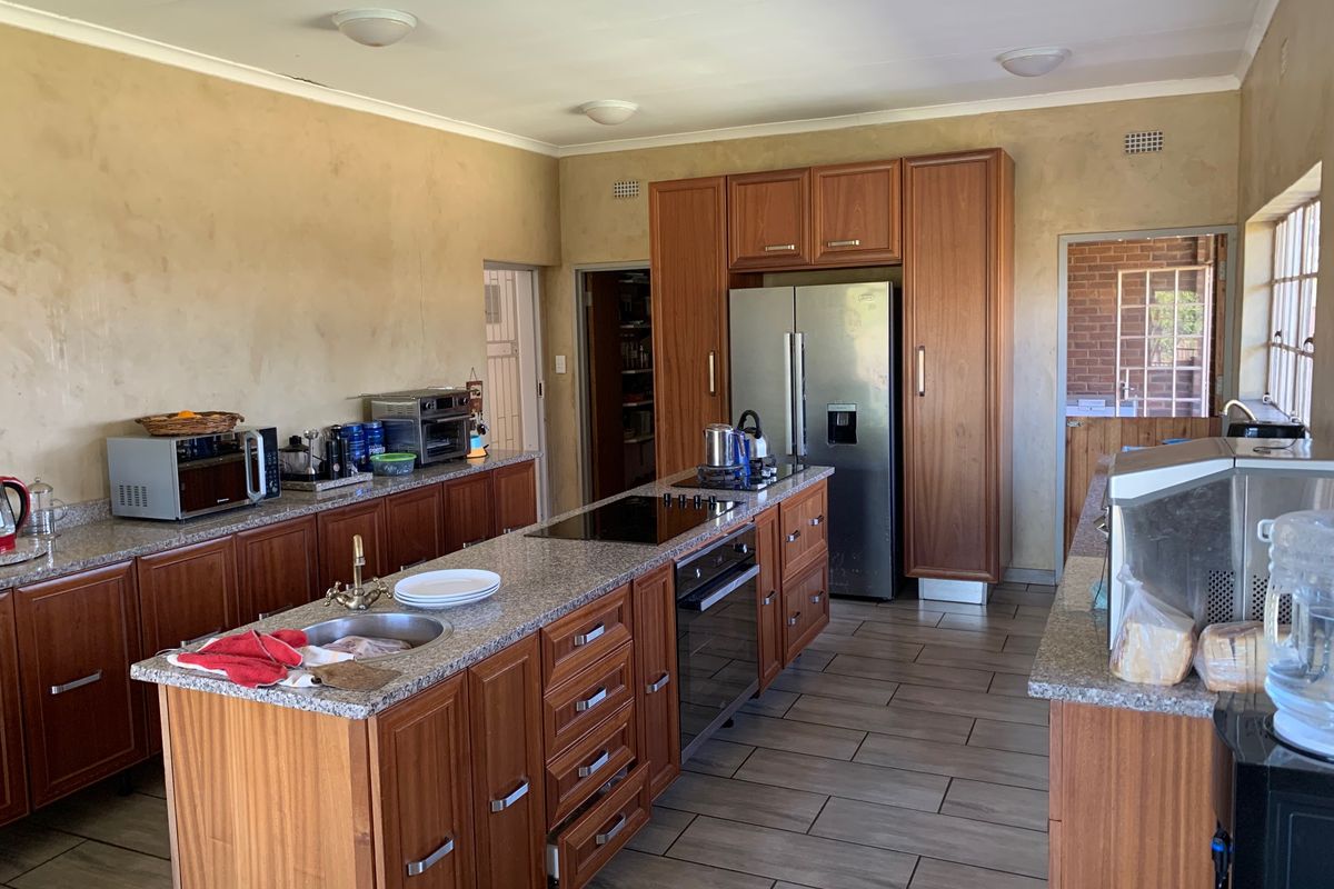 Spacious kitchen featuring wooden cabinetry, granite countertops, a central island with a built-in oven and hob, and tiled flooring.