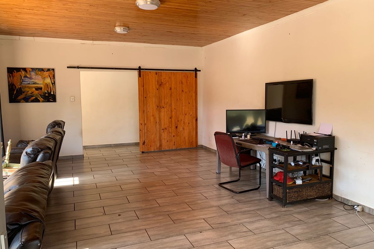 Spacious living area featuring a warm timber ceiling, ceramic floor tiles, and a rustic sliding barn door leading to an adjacent room.