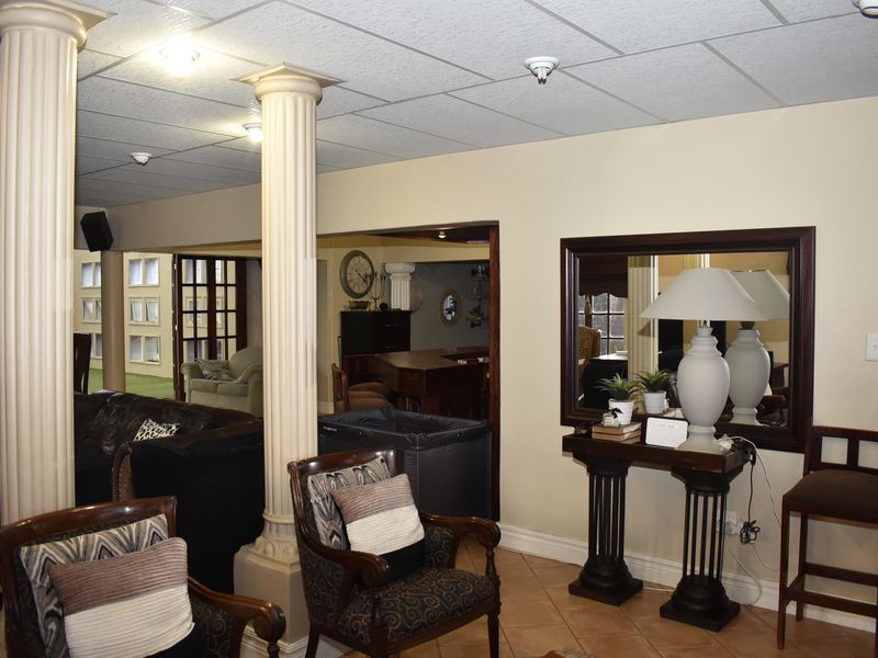 Spacious living area featuring decorative columns, suspended ceiling tiles, and tiled flooring, offering a versatile layout for relaxation and entertaining.