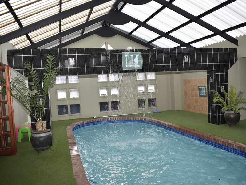 Indoor swimming pool area featuring a built-in water feature, translucent roof structure, and glass block windows, providing a unique enclosed recreational space.