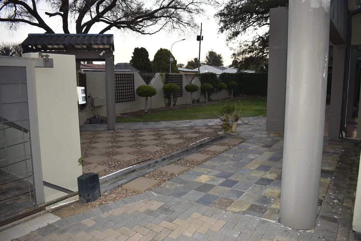 Rear exterior area featuring a paved patio, boundary wall, and landscaped garden space with structural columns.
