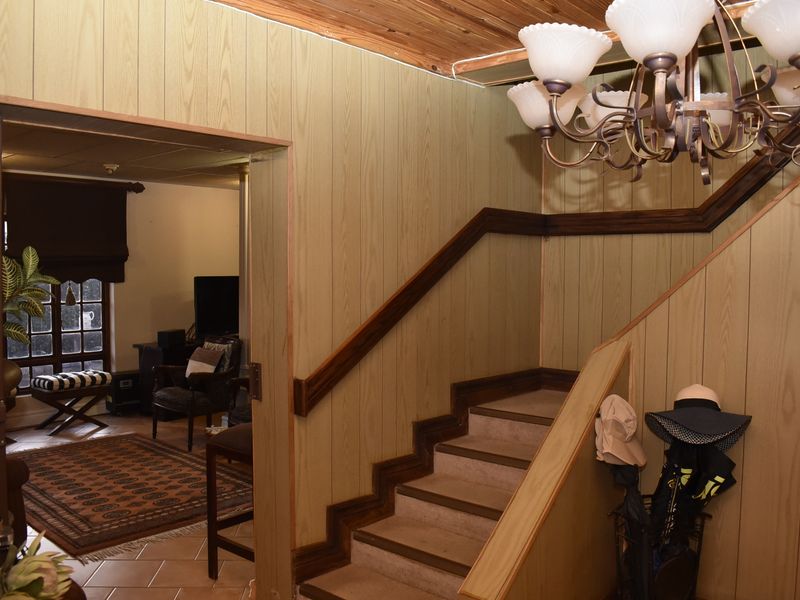 Entrance hallway featuring a staircase with timber handrails, wood-paneled walls, and a timber ceiling, leading into an adjacent living area.