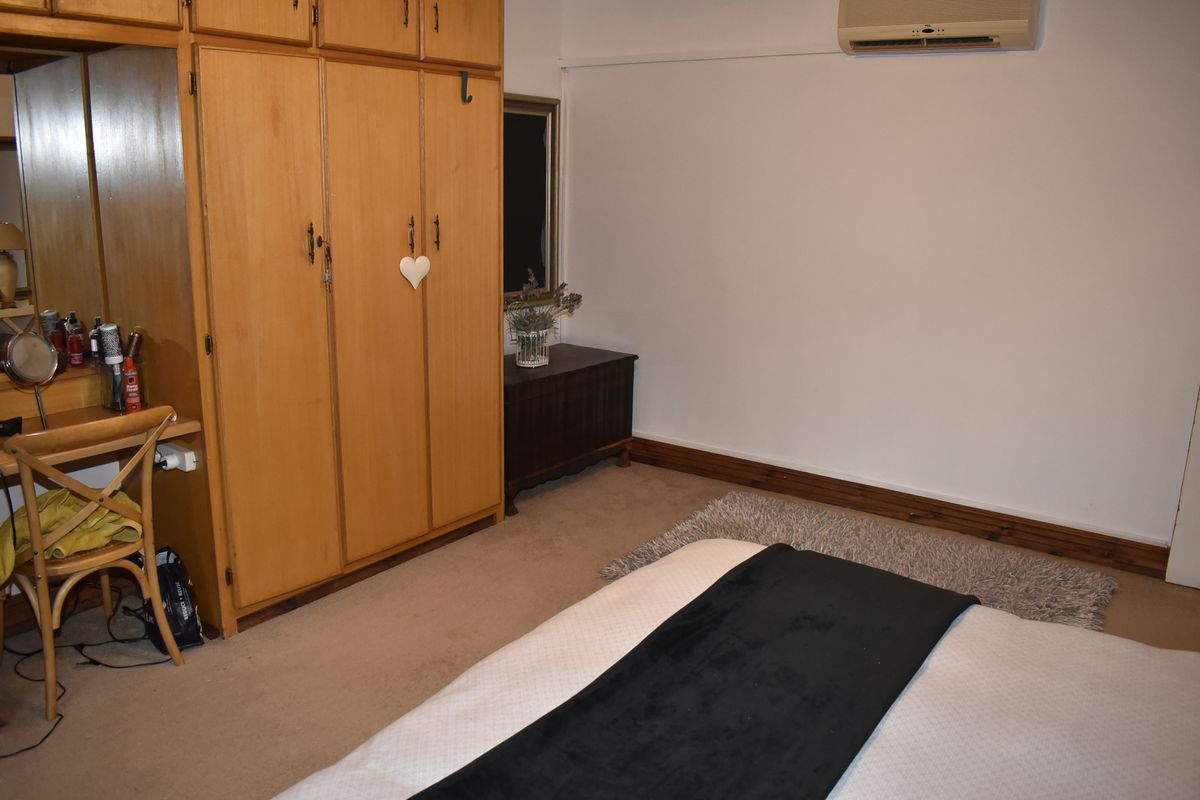 A bedroom featuring built-in wooden cupboards, carpeted flooring, and a wall-mounted air conditioning unit.