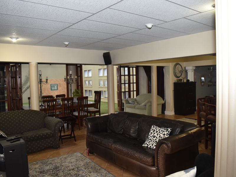 Spacious open-plan living and dining area featuring tiled flooring, structural columns, and a drop ceiling, with direct access to an outdoor patio space.